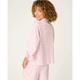 A woman with curly brown hair is shown from the back wearing a light pink pajama set with a small green leaf pattern, photographed against a clean off-white studio background.