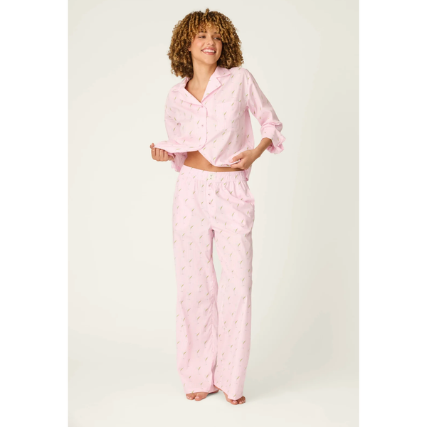 A woman modeling a light pink pajama set with a small repeating floral pattern, consisting of a long-sleeve button-up shirt and matching wide-leg pants, against a plain light background.