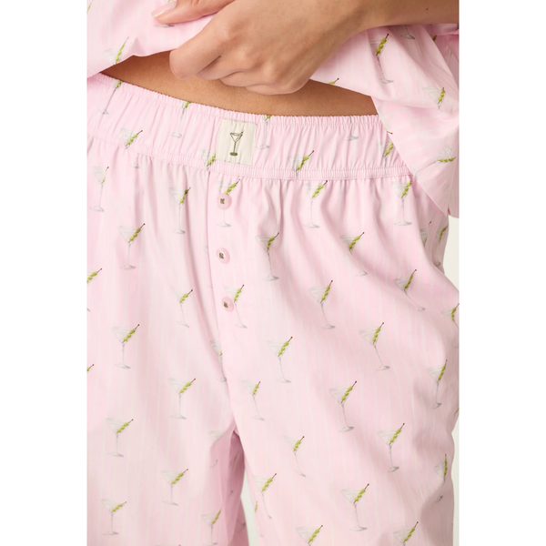 Close-up of a person wearing light pink pajama pants with an allover small cocktail print and a matching top, shown against a plain light background.