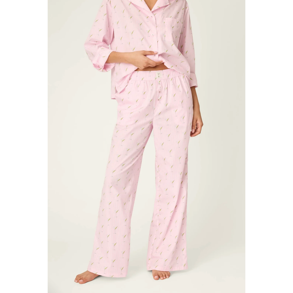 A model wearing a light pink two-piece pajama set with a small green leaf pattern, featuring a long-sleeve button-up shirt and matching wide-leg pants, photographed against a clean off-white studio background.