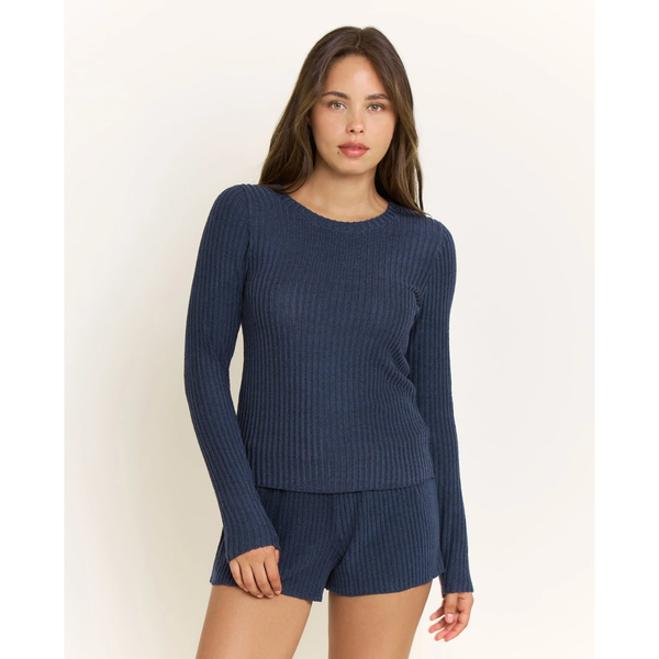 A woman modeling a matching navy blue ribbed knit lounge set, consisting of a long-sleeve top and shorts, against a plain off-white background.