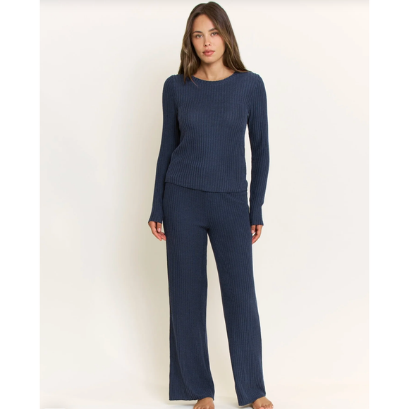 A woman modeling a matching ribbed knit lounge set in dark navy blue, consisting of a long-sleeve crewneck top and wide-leg pants, against a plain off-white studio background.