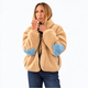A woman wearing a beige sherpa fleece jacket with light blue elbow patches, paired with blue jeans, photographed against a solid white background.