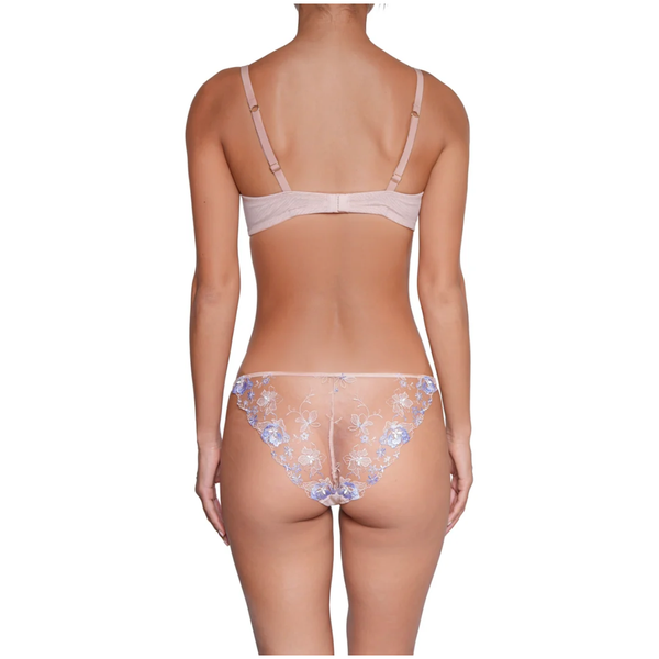Rear view of a model wearing a light beige bra and matching panties with blue floral lace detailing, set against a plain white background.