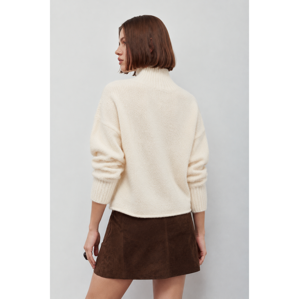 A woman shown from the back wearing a cream-colored fuzzy mock-neck sweater and a brown mini skirt, against a plain light gray background.