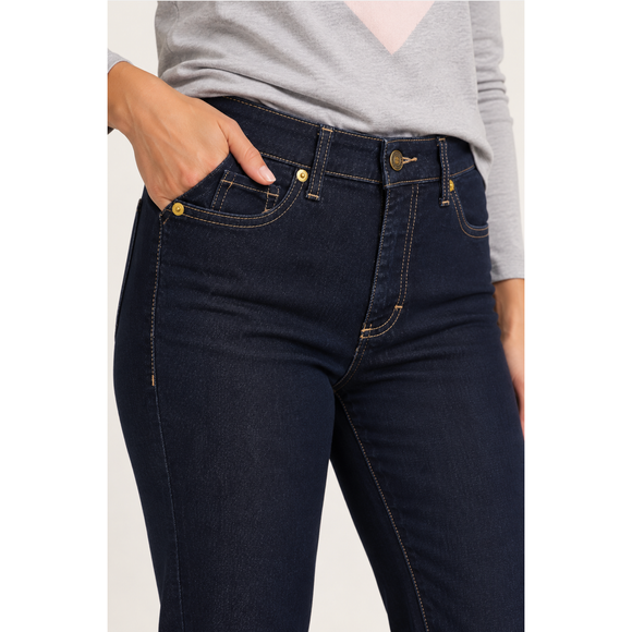 Close-up of a person wearing dark indigo skinny jeans with gold-tone hardware and a light gray long-sleeve top, with one hand in the pocket.