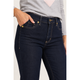 Close-up of a person wearing dark indigo skinny jeans with gold-tone hardware and a light gray long-sleeve top, with one hand in the pocket.