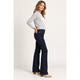 A woman modeling dark blue flared jeans with a light gray long-sleeve top and beige heels, standing against a plain light gray studio background.
