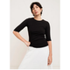 A model wearing a black 3/4-sleeve crewneck top and white skirt, posing against a plain off-white studio background.