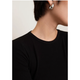 Close-up of a person wearing a black ribbed crew-neck top and a shiny silver teardrop-shaped earring against a plain light background.