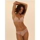 A woman modeling a light beige/nude lace bra and matching lace underwear against a plain beige studio background.
