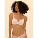 A woman modeling a pale pink underwire bra and matching lace panties against a solid cream background.