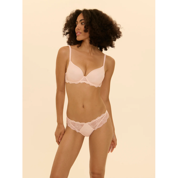 Woman wearing a light pink bra and underwear set on a beige background