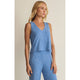 Woman wearing a blue sleeveless top and pants against a beige background