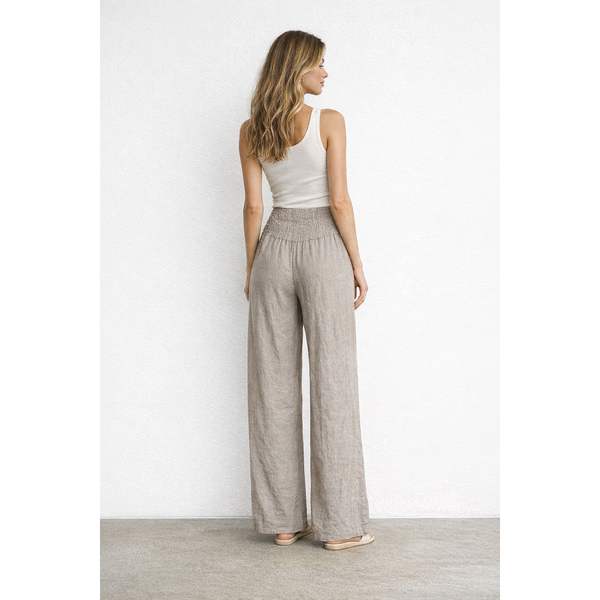 Woman wearing a white tank top and beige wide-leg pants against a white wall.