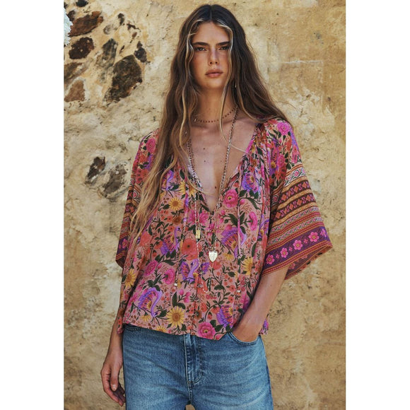 Woman wearing a colorful floral blouse with a stone wall background