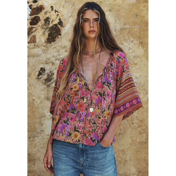 Woman wearing a colorful floral blouse with a stone wall background