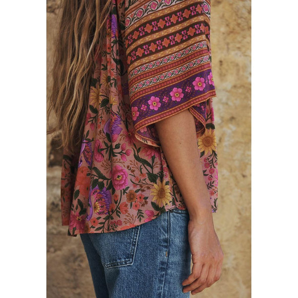 Person wearing a colorful floral and striped top against a stone wall background