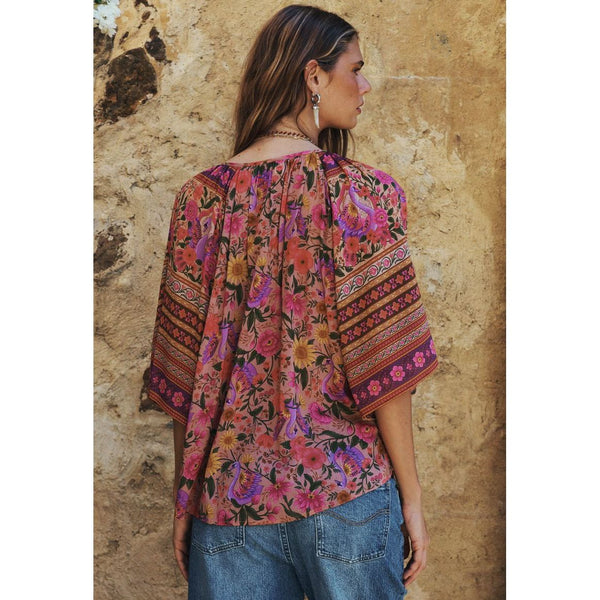 Woman wearing a colorful patterned top against a stone wall.