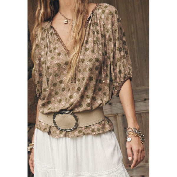 Woman wearing a floral blouse with a belt and white pants in a rustic setting