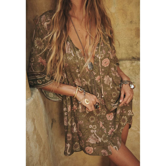Person wearing a floral dress with jewelry against a textured wall.