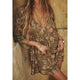 Person wearing a floral dress with jewelry against a textured wall.