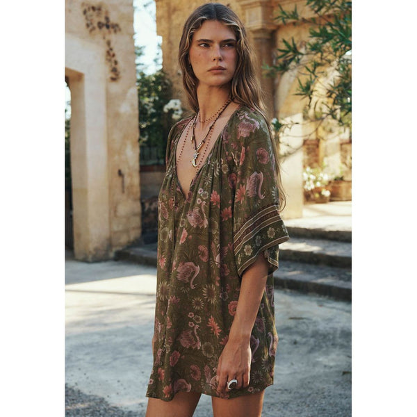 Woman wearing a patterned dress standing in an outdoor setting with stone architecture.
