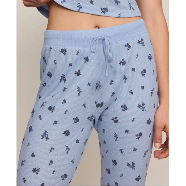 A close-up of a person wearing light blue waffle-knit pajama pants with a small dark floral print and a matching drawstring waist, paired with a matching cropped top.