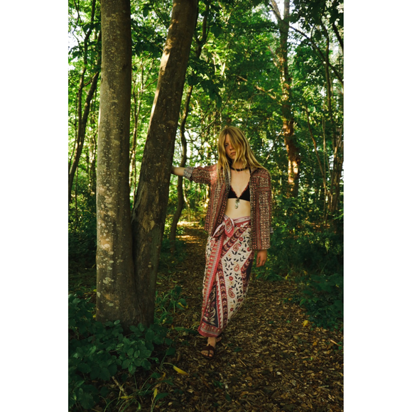 Woman in a patterned sarong and jacket standing in a forest
