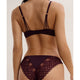 Rear view of a model wearing a dark plum lace bralette with strappy back details and matching lace thong against a plain light beige background.