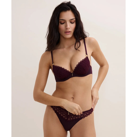 Woman wearing a dark red lace lingerie set against a plain background