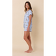 A woman modeling a light blue short-sleeve pajama set with a delicate floral pattern, standing against a solid beige studio background.