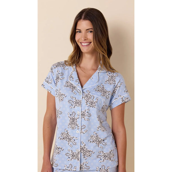 A woman wearing a light blue short-sleeve pajama top with a brown and beige floral pattern, set against a solid beige background.