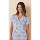A woman wearing a light blue short-sleeve pajama top with a brown and beige floral pattern, set against a solid beige background.