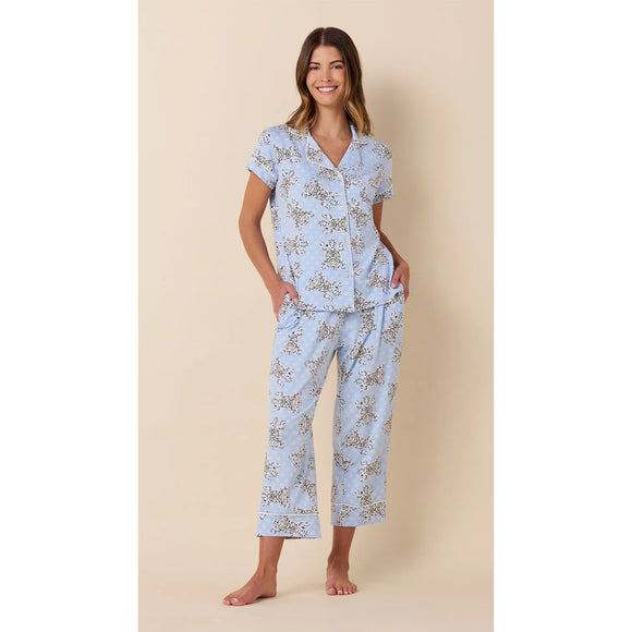 A woman modeling a light blue short-sleeve pajama set with a delicate floral print, standing against a solid beige background.