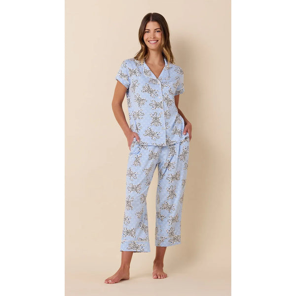 A woman modeling a light blue short-sleeve pajama set with a delicate floral print, standing against a solid beige background.