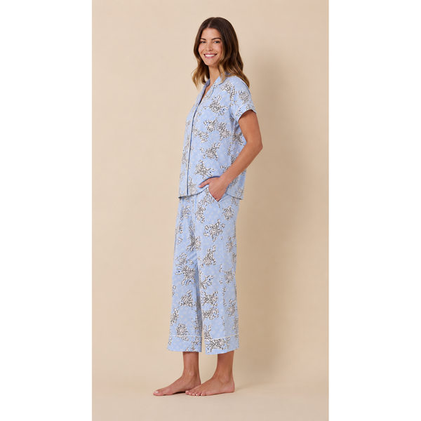 A woman modeling a light blue pajama set with a delicate beige floral pattern, standing against a solid beige background.
