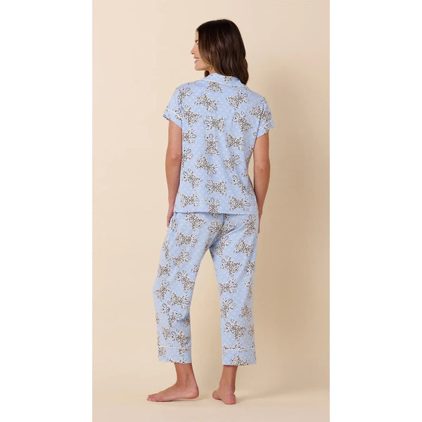 A woman shown from the back wearing a light blue pajama set with a delicate beige and brown floral pattern, standing against a solid beige background.