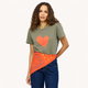 A woman modeling an olive green t-shirt with a large orange heart on the front, paired with blue jeans and an orange patterned bandana tied around her waist, against a plain off-white background.