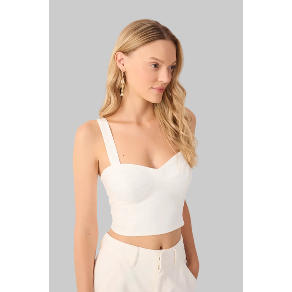 Woman wearing a white crop top and pants on a plain background