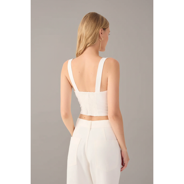 Woman wearing a white sleeveless top and pants on a light background