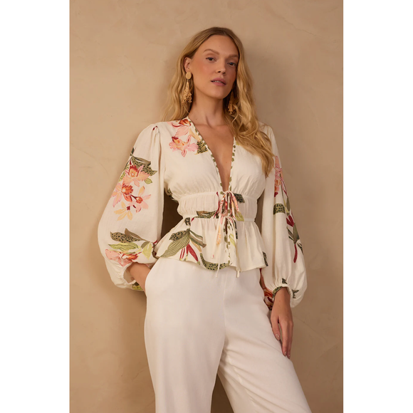 Woman wearing a floral blouse and white pants against a beige background