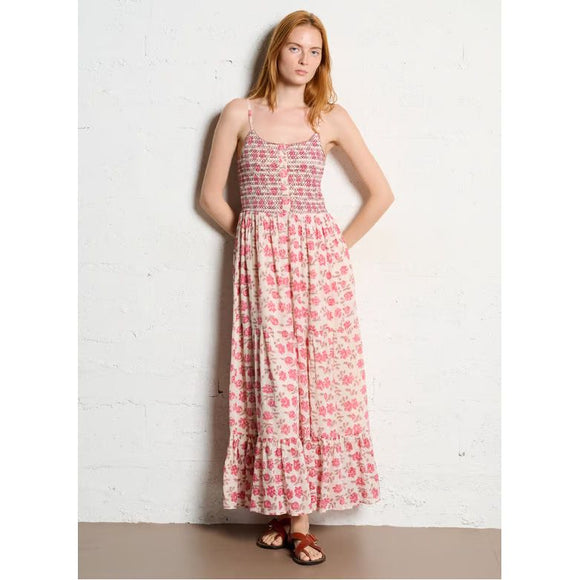 Woman wearing a pink floral dress against a white brick wall.