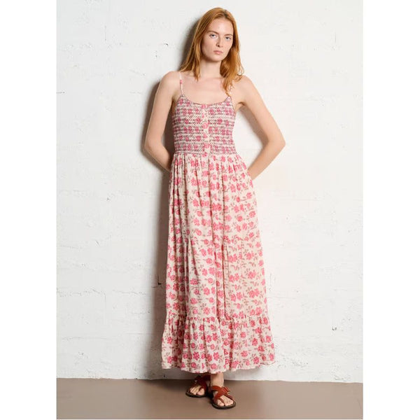 Woman wearing a pink floral dress against a white brick wall.