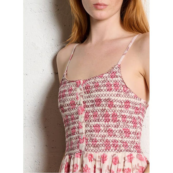 Woman wearing a pink and white patterned dress against a white wall.