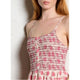 Woman wearing a pink and white patterned dress against a white wall.