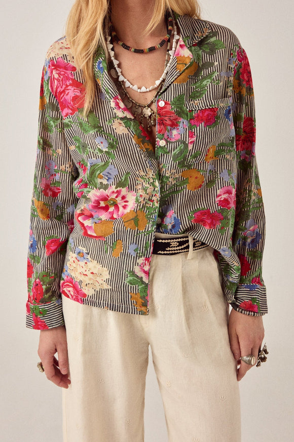 Person wearing a colorful floral and striped shirt with beige pants on a plain background