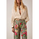 Person wearing a beige lace blouse and floral pants on a plain background