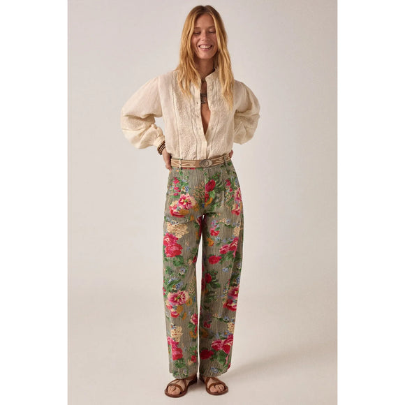 Woman wearing a cream blouse and floral pants on a plain background