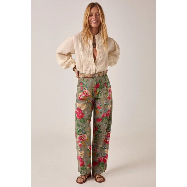 Woman wearing a cream blouse and floral pants on a plain background